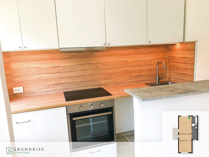 Foto einer modernen Küche mit Holzfronten und Kücheninsel, in deren rechter unterer Ecke ein kleiner Grundriss mit farblicher Markierung des Küchenbereichs eingeblendet ist.