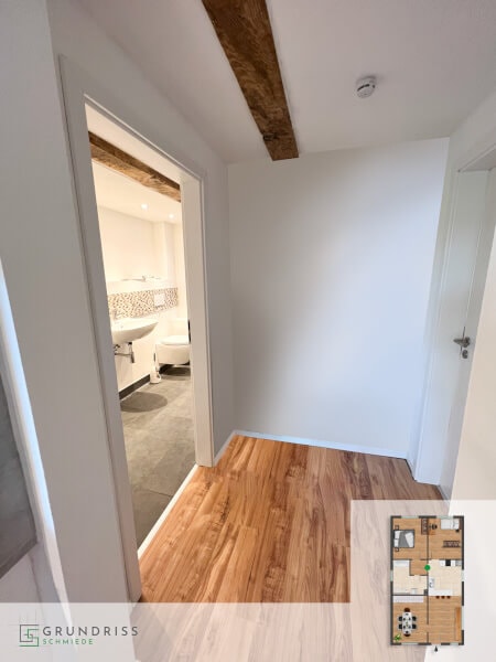 Foto eines Flurs mit Blick durch die geöffnete Tür in ein modernes Badezimmer, in der rechten unteren Ecke ein eingeblendeter Erdgeschoss-Grundriss mit farblicher Markierung des Flurbereichs.