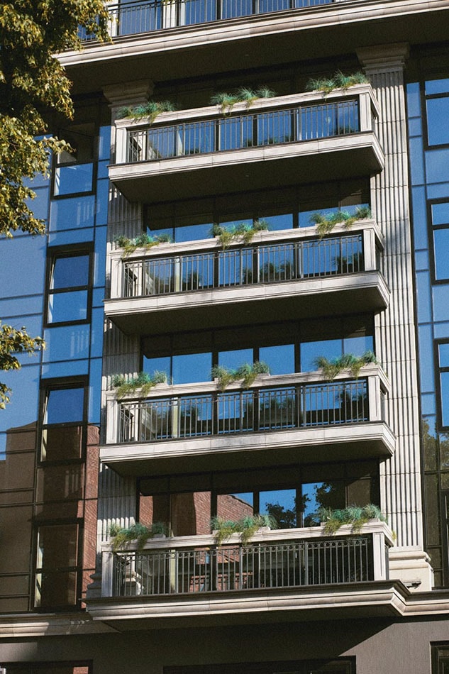 Es sind vorgesetzte Balkone mit schwarzem Geländer an der Glasfassade eines mehrgeschossigen Gebäudes zu sehen.