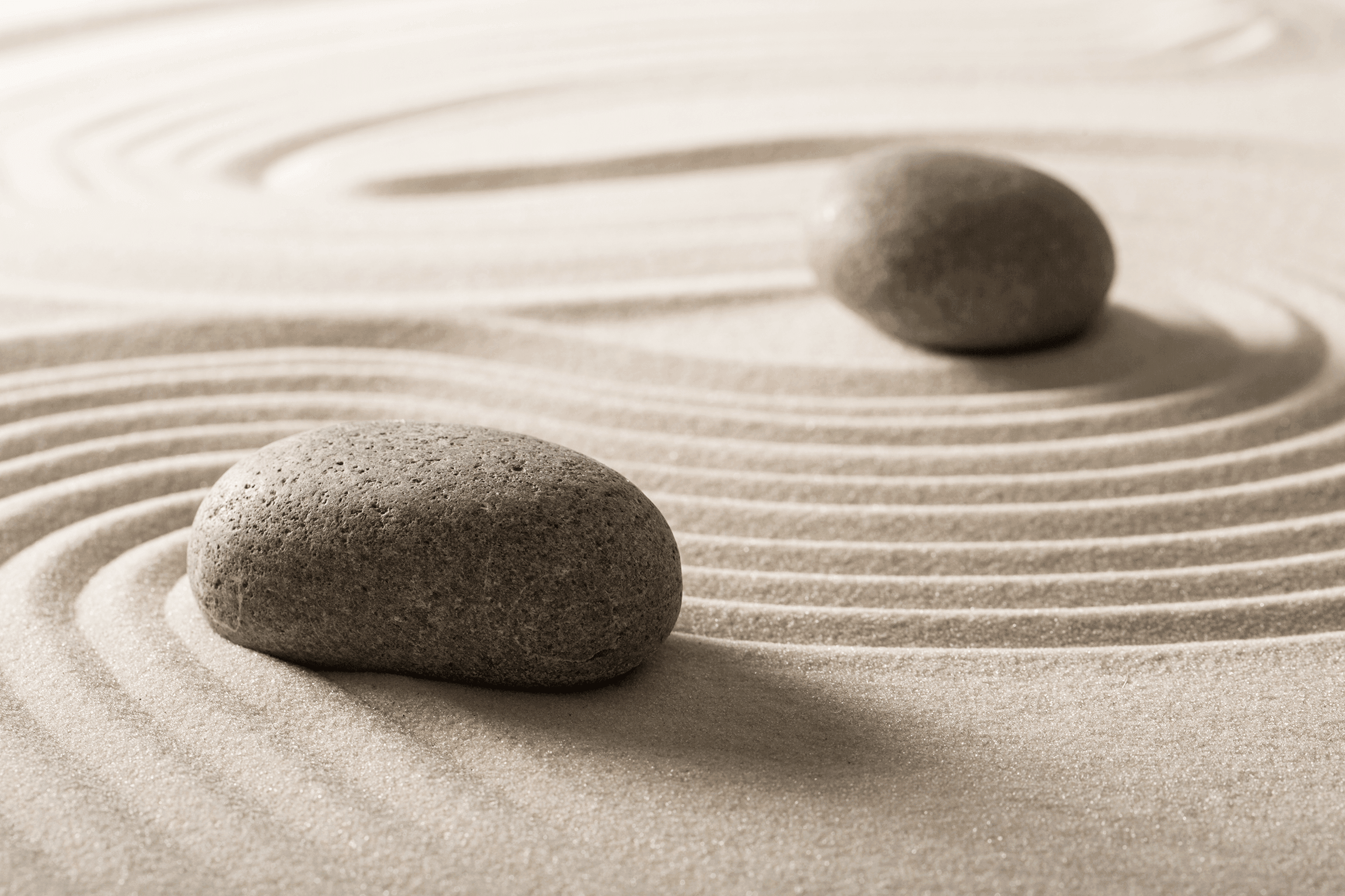 Zwei glatte Steine im Zen-Garten mit konzentrischen Rillenmustern im Sand als Symbol für Harmonie und Gleichgewicht.