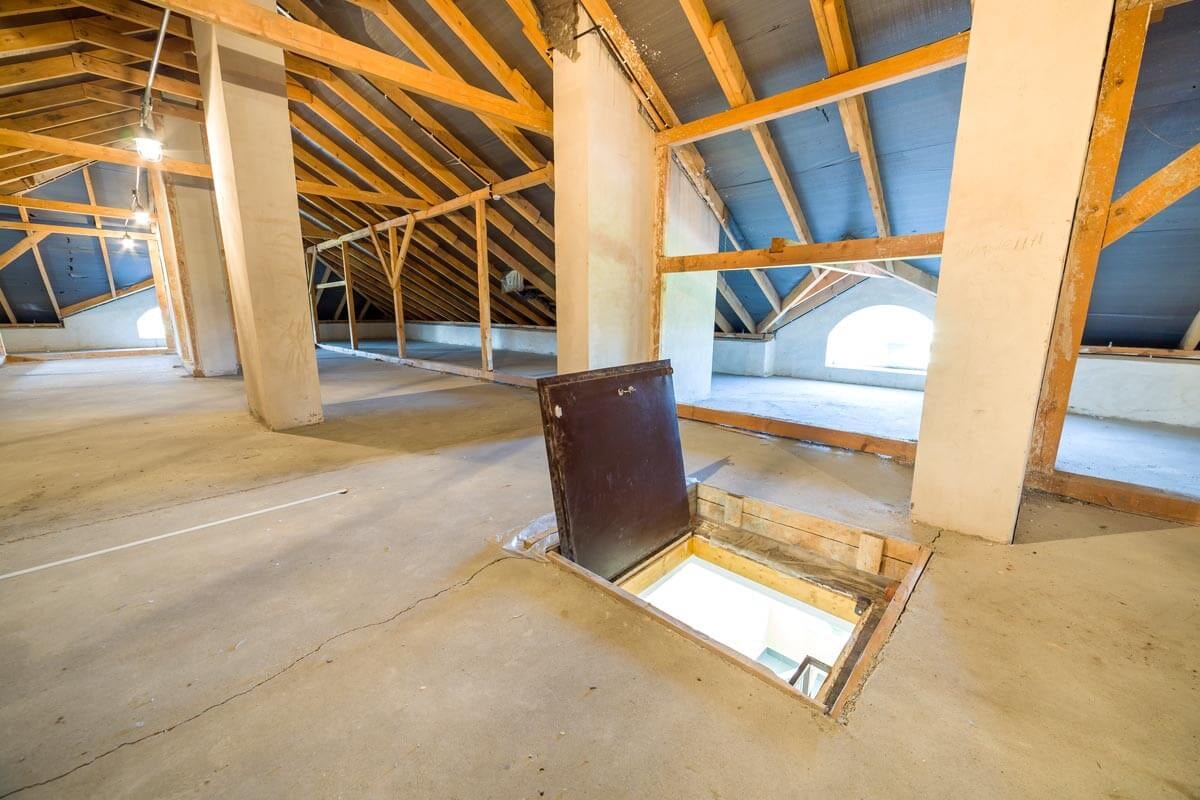 Nicht ausgebauter Dachboden mit Dachstuhl-Konstruktion aus Holz und Leiterschacht nach unten.