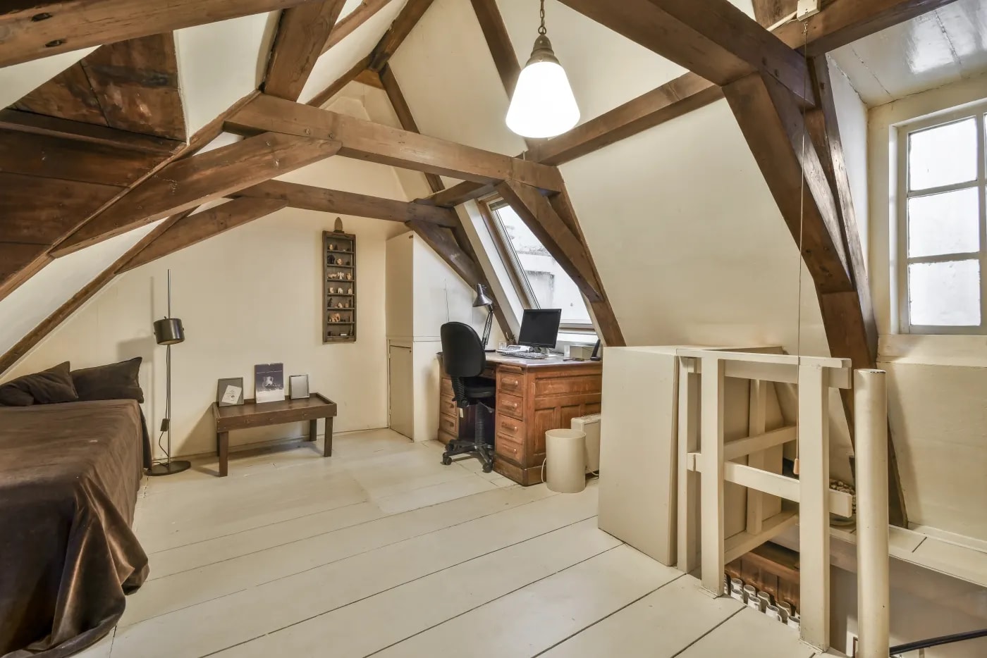 Blick aus der Ecke eines Raumes auf einen ausgebauten Dachstuhl eines hohen Satteldachs mit Gebälk und Dachfenstern.