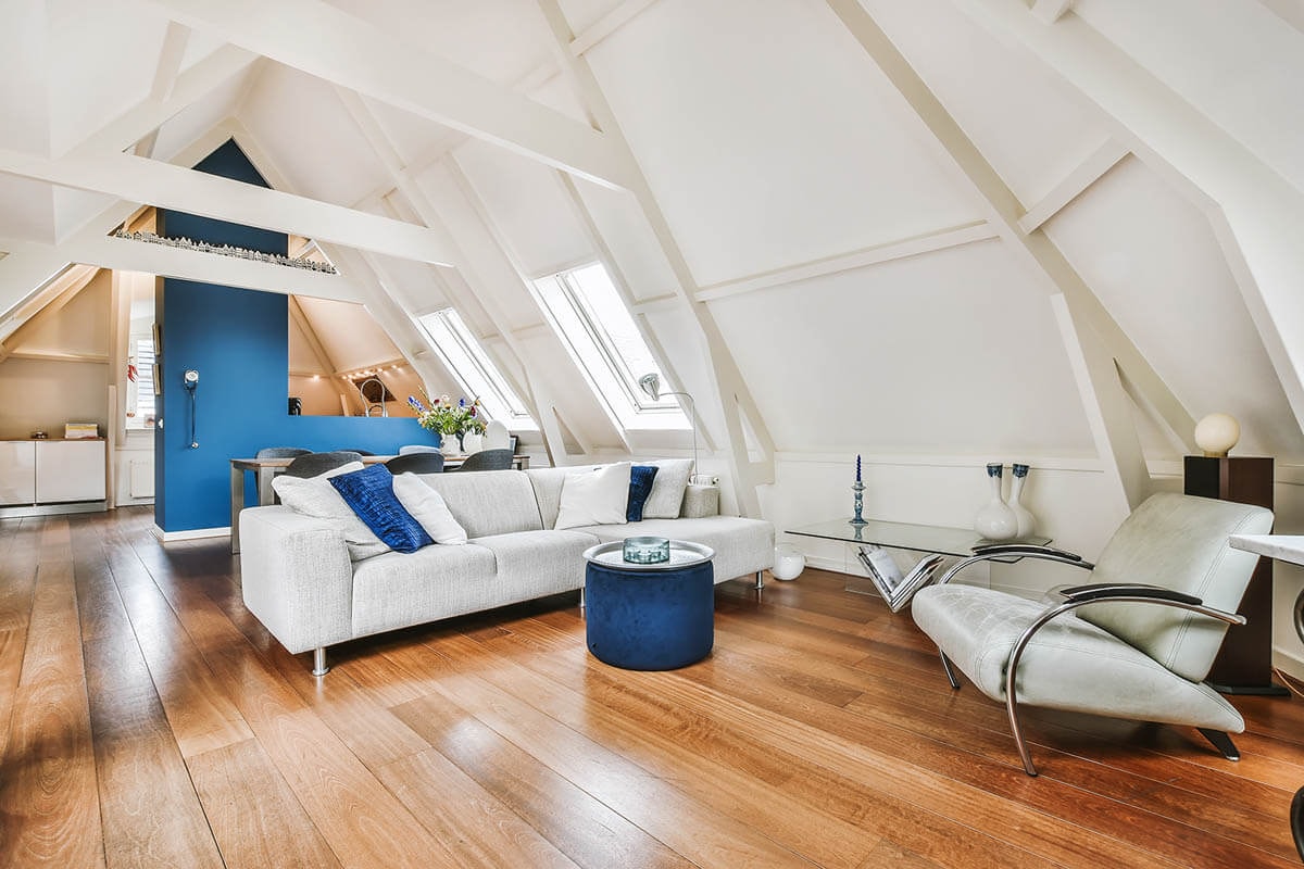 Ausgebauter Dachstuhl mit Holzfußboden, vorne ein Wohnzimmer dahinter eine offene Küche erkennbar.