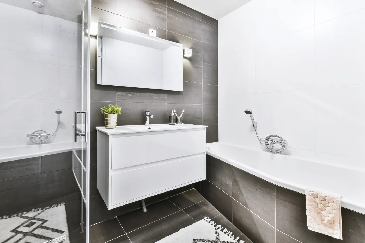 Modernes Badezimmer in Schwarz-Weiß-Optik mit kombinierter Badewanne und Dusche, hängendem Waschbeckenschrank und spiegelnder Tür.