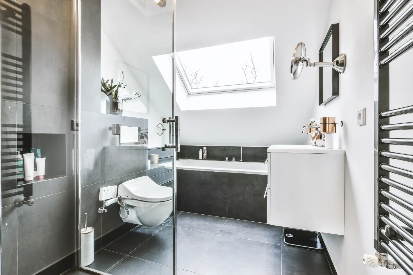 Modernes Badezimmer in Schwarz-Weiß-Optik mit Wanne unter einer Dachschräge, hängendem WC und Waschbeckenschrank, sowie Heizgitter für Handtücher an der Wand.