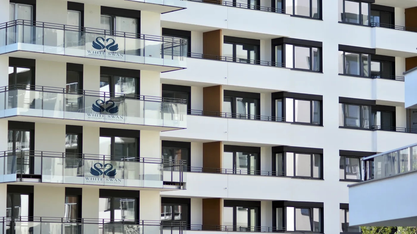 Detailaufnahme von der Fassade des 'White Swan'-Objekts mit Balkonen auf denen das Logo des Objekts auf der Glasplatten-Umrandung zu sehen ist.