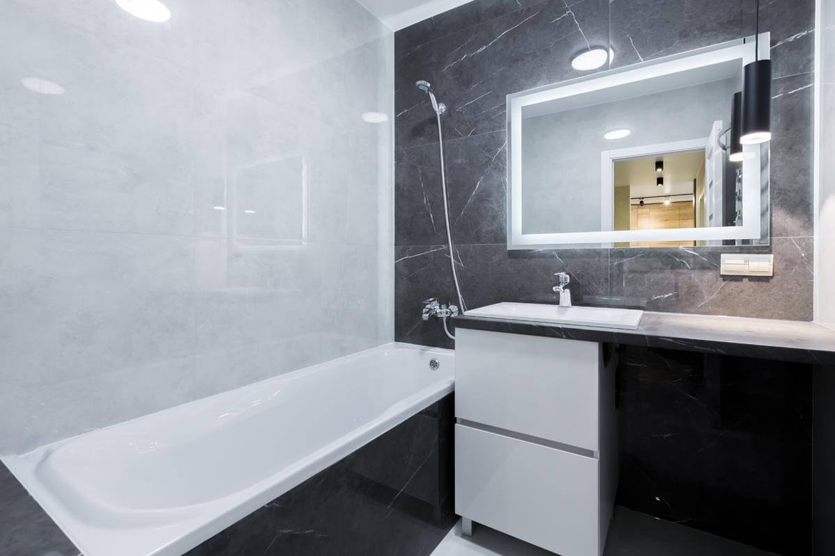 Kleines, modernes Badezimmer in Schwarz-Weiß-Optik mit kombinierter Dusche und Badewanne und Waschbecken mit großem Spiegel darüber.