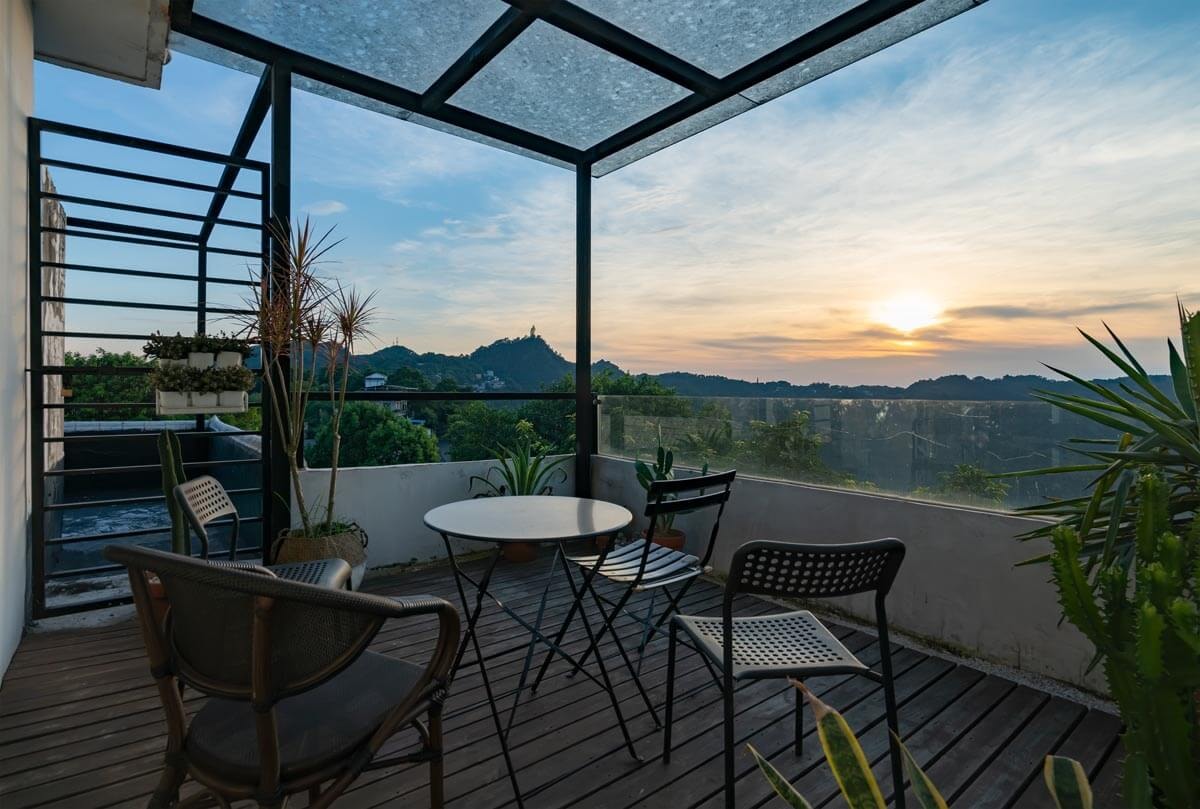 Sitzgruppe und Pflanzen auf einer Terrasse mit Acryldach und Sonnenuntergangsstimmung.