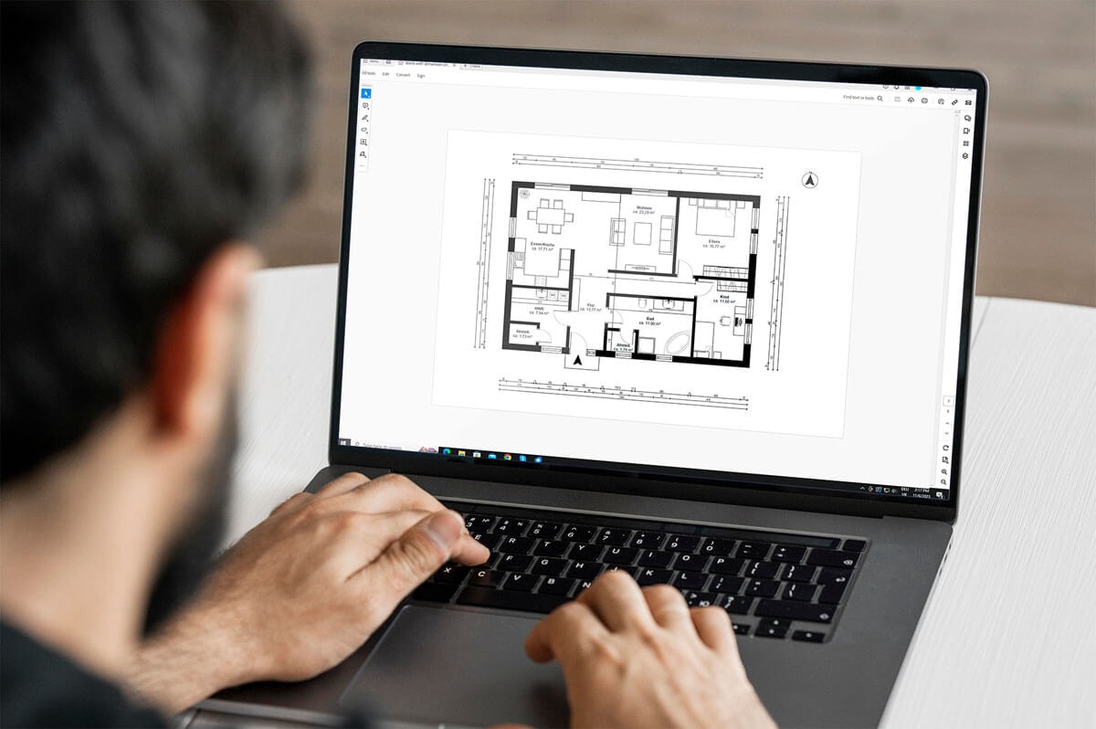 Ansicht von hinten: ein Mann sitzt an einem Laptop mit der hand auf der Tastatur und betrachtet den bemaßten Grundriss einer 3,5-Zimmer Wohnung.