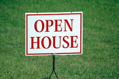 Auf einem grünem, gepflegten Rasen steht ein weißes Schild mit roter Aufschrift: 'Open House'.