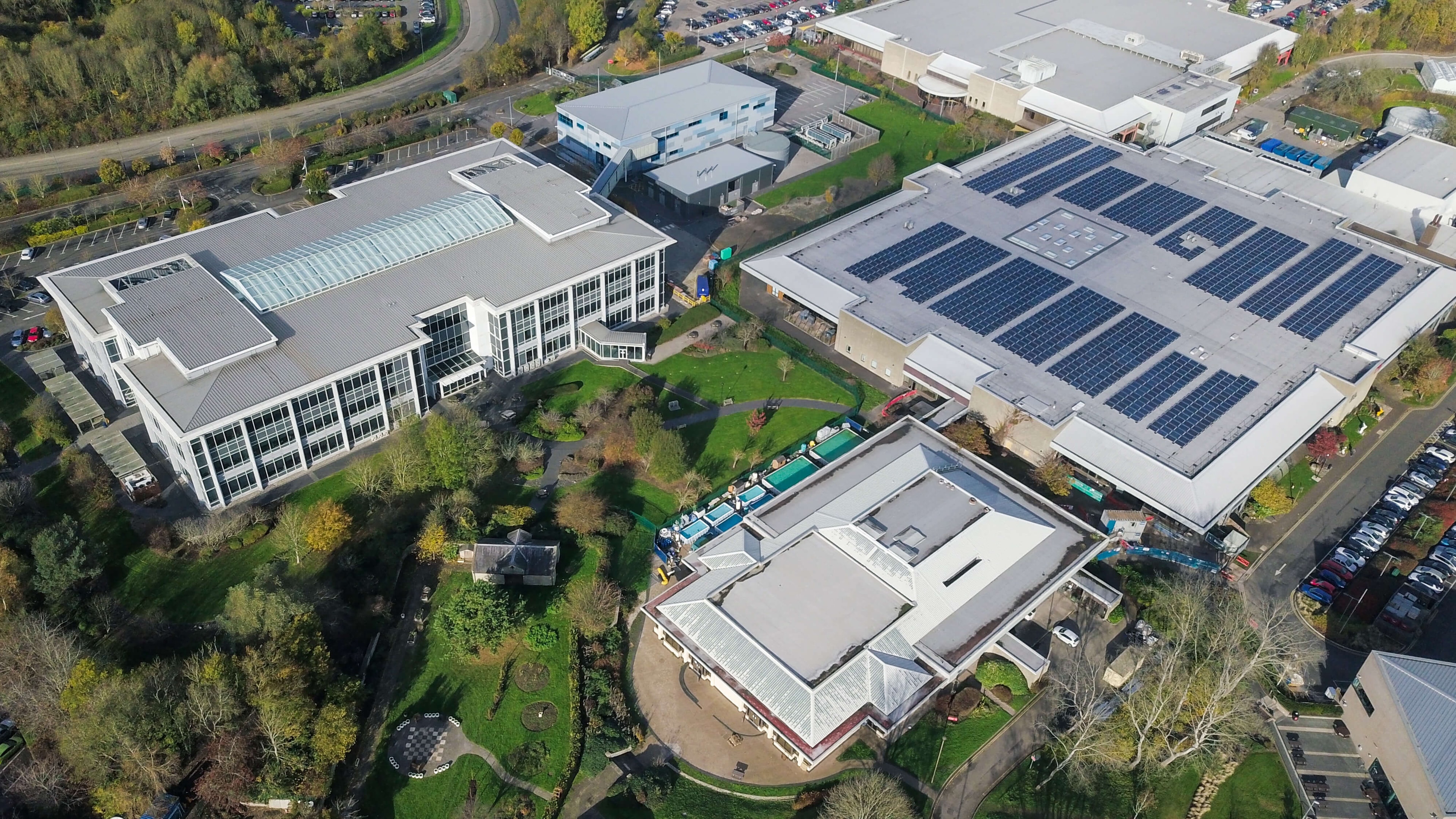Luftaufnahme eines größeren, industriellen Gebäudekomplexes von dem eines der Gebäude Solarpanels auf dem Dach hat.