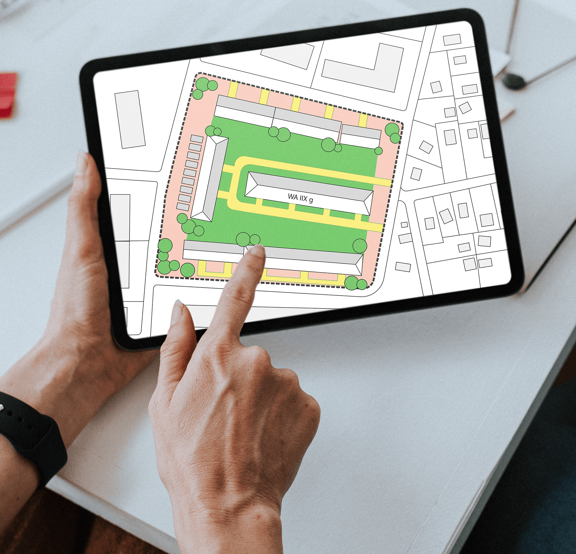 Nahaufnahme von einem Tablet, das einen kolorierten Bebauungsplan eines Bürogebäude-Komplexes zeigt, der an einer Grünfläche gelegen ist und rundherum Parkplätze ausweist.
