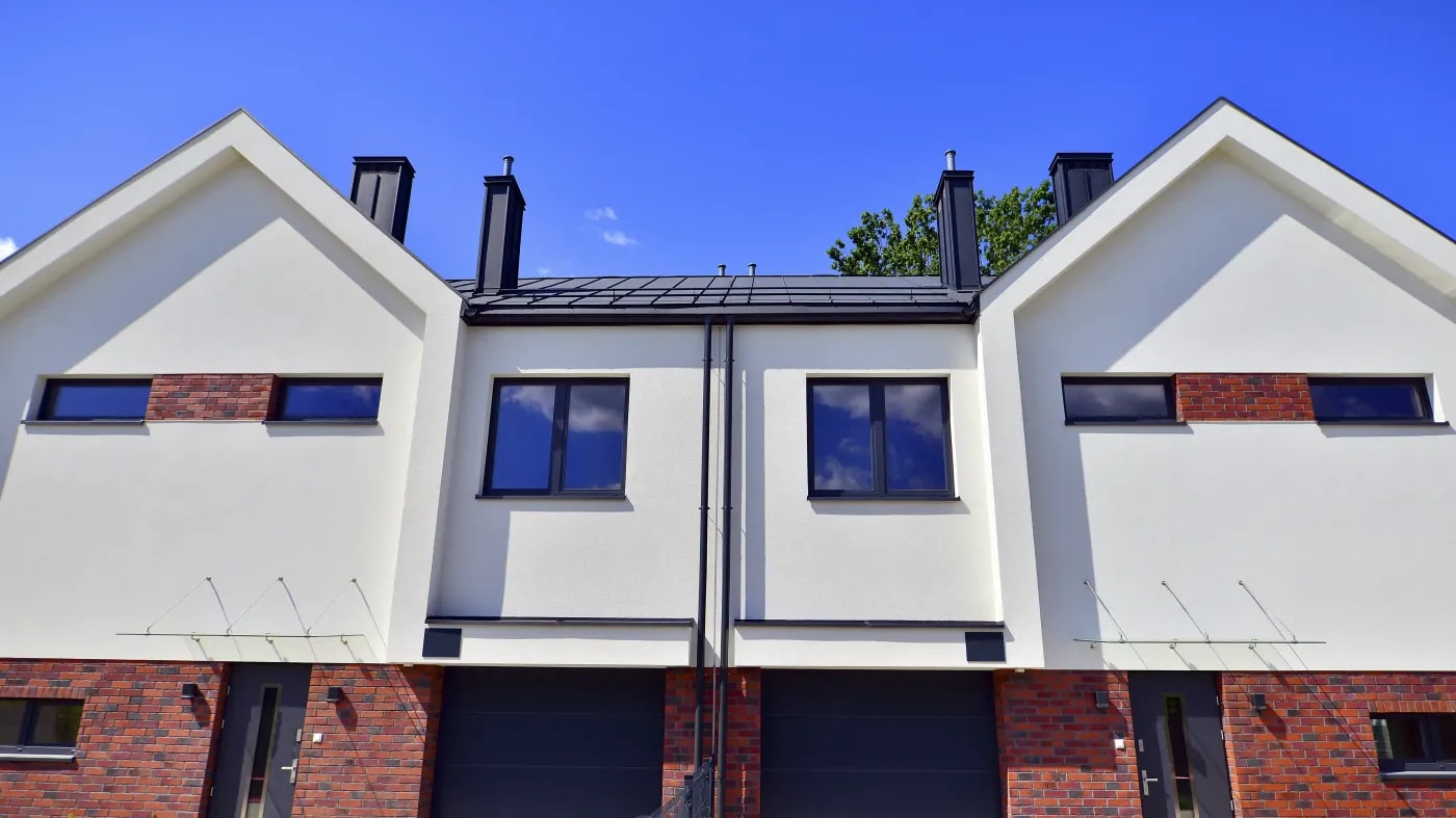 Modernes, symmetrisches Doppelhaus mit Klinker- und Putzfassade, Garagen neben den Eingängen, Satteldach und einem Fenster an der Front.