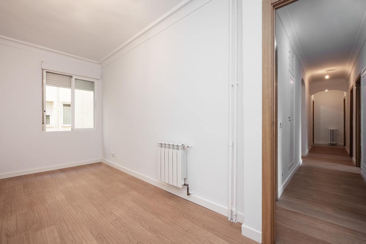 Blick aus der Ecke eines Raumes in den langen Flur einer leeren Wohnung mit Laminatfußboden und weißen Wänden.