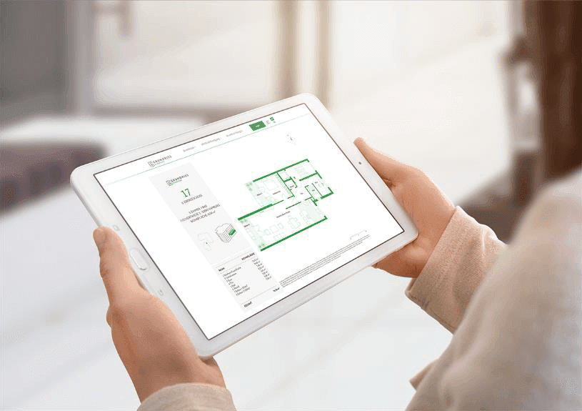 Ein Tablet wird hoch gehalten und darauf befindet sich die Ansicht eines Grundrissschmiede Factsheets für das 2. Obergeschoß eines mehrgeschossigen, Mehrfamilienhauses von dem eine 3-Zimmer Wohnung zu sehen ist.