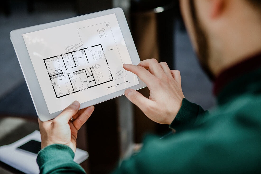 Blick über die Schulter eines Mannes, der ein Tablet hoch hält und mit der rechten Hand versucht etwas auf dem Screen zu schieben.