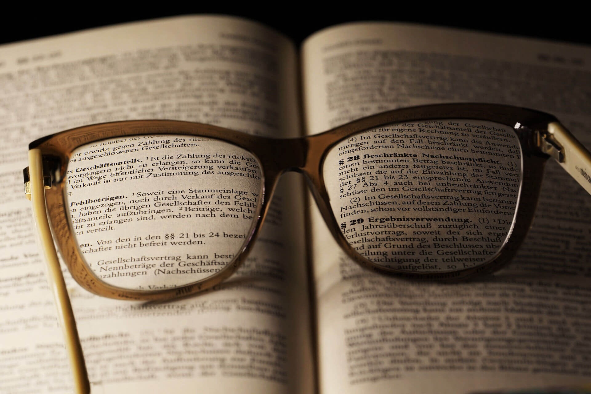 Nahaufnahme eines Buches mit Gesetzestexten und offener Brille darauf, die einige Texte deutlicher sehen lässt.
