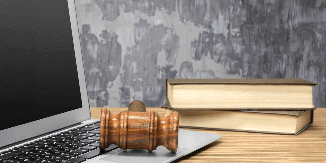 Nahaufnahme eines Laptops auf einem Tisch, neben dem ein Auktionshammer aus Holz und zwei gestapelte Bücher liegen.