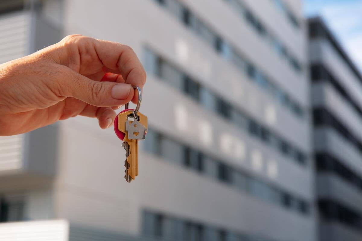 Hand hält einen Bund Hausschlüssel vor unscharfem Außenbereich; Symbolbild für Wohnungsübergabe und Mietverhältnis.