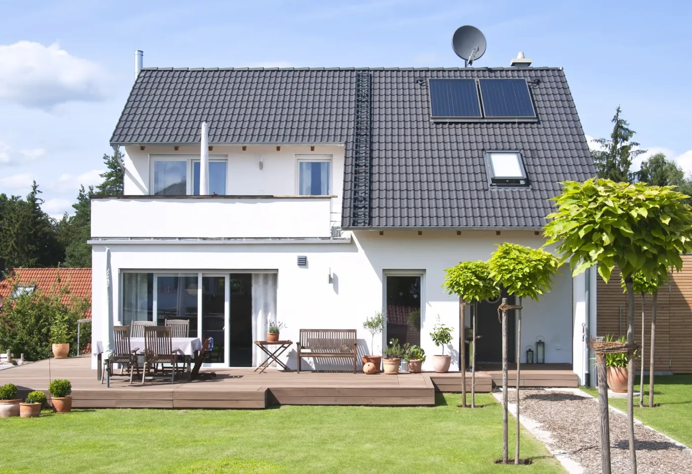 Modernes Einfamilienhaus mit zwei Etagen, Balkon, Terrasse und Satteldach, sowie Solarpanele auf dem Dach, das von Rasen umgeben ist.