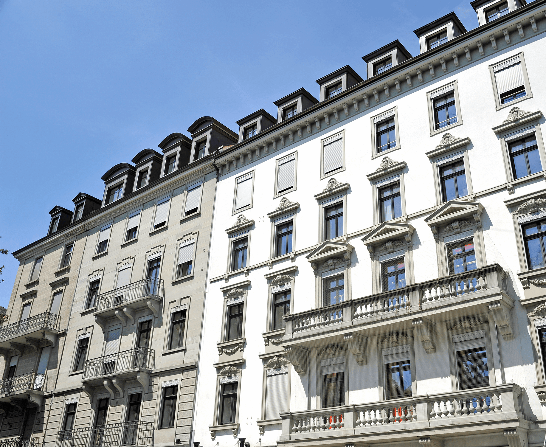 Aufnahme schräg von unten mit Sicht auf die obere linke Hausecke eines städtischen Altbau-Reihenhauses mit Zierfassade und Balkonen.