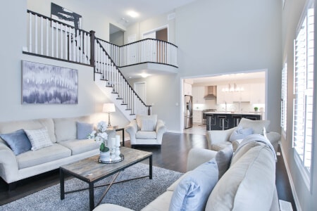 Gestyltes Wohnzimmer mit zwei weißen Sofas, rustikalem Holzcouchtisch und einer Treppe mit schwarzem Geländer; im Hintergrund Blick in eine Küche.