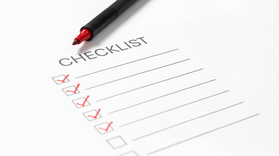 Eine ausgedruckte Checkliste auf der ein offener, roter Stift liegt und einige Punkte mit einem roten Haken versehen sind.