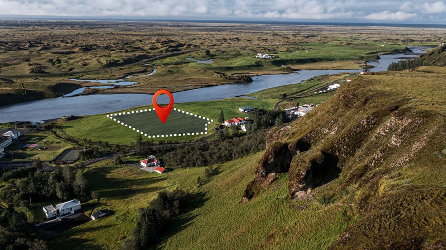 Photo einer Flußlandschaft von einem Hügel herunter, in dem schematisch mit weißer gestrichelter Linie die Umrisse eines nahezu rechteckigen Grundstücks eingezeichnet und mit einem roten Tropfenmarker gekennzeichnet sind.