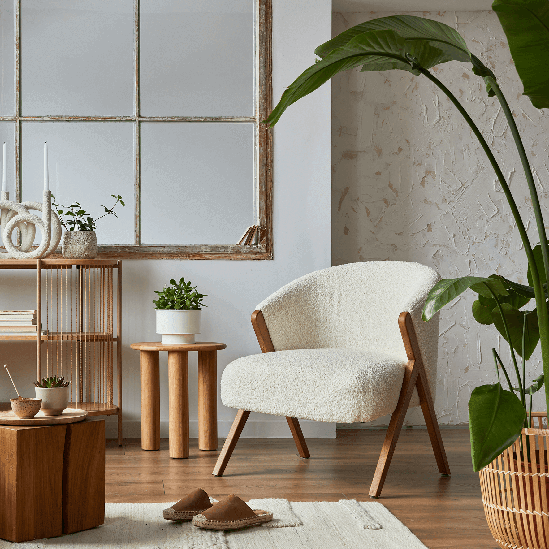 Wohnzimmer-Ecke im Boho-Stil mit weißem Bouclé-Sessel, großer Zimmerpflanze, Holzregal mit Dekorationsobjekten und antikem Spiegel.