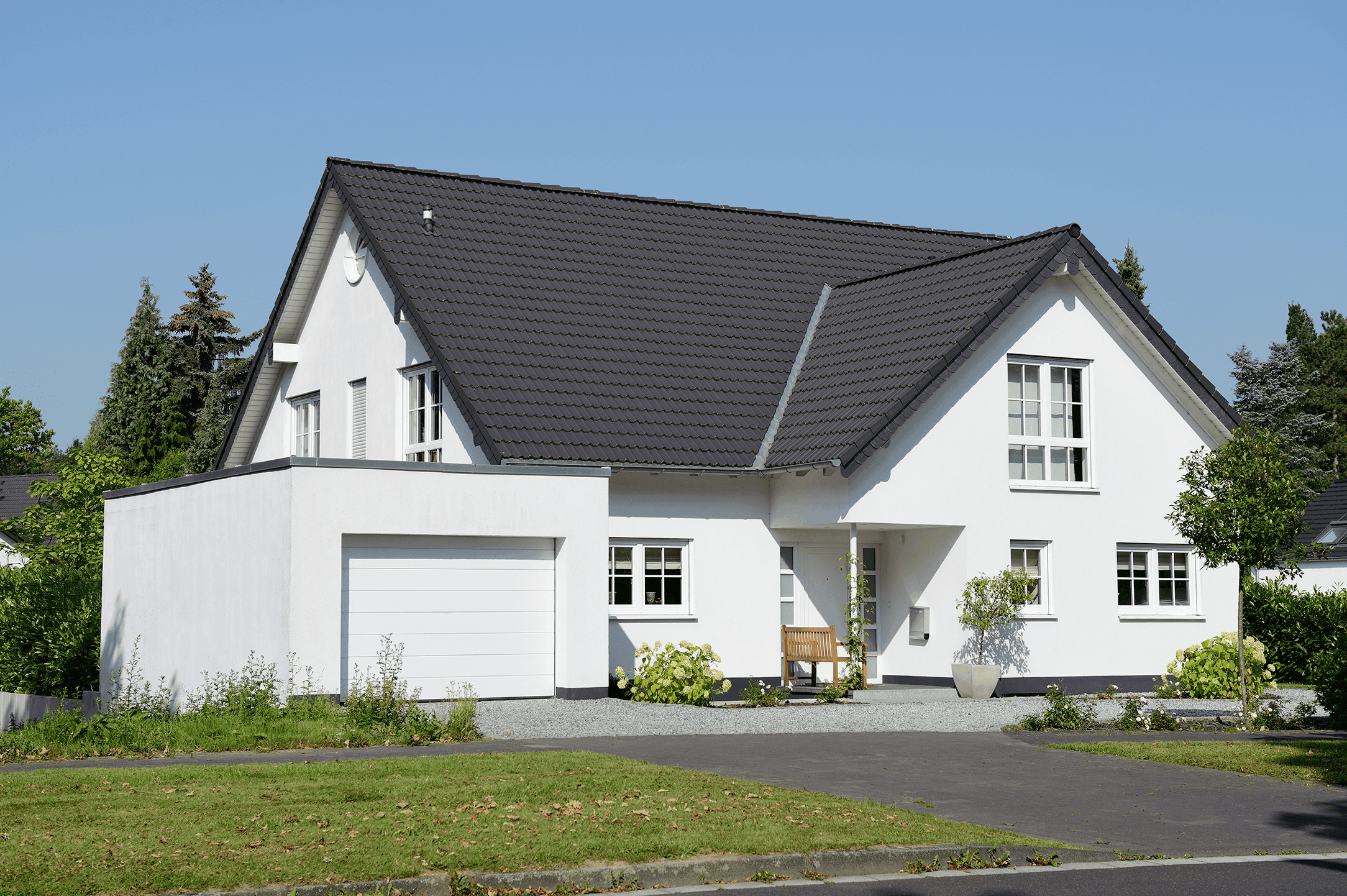 Aussenansicht eines mehrgeschossigen, modernen Einfamilienhauses mit L-Form, Garage und dunklem Satteldach.