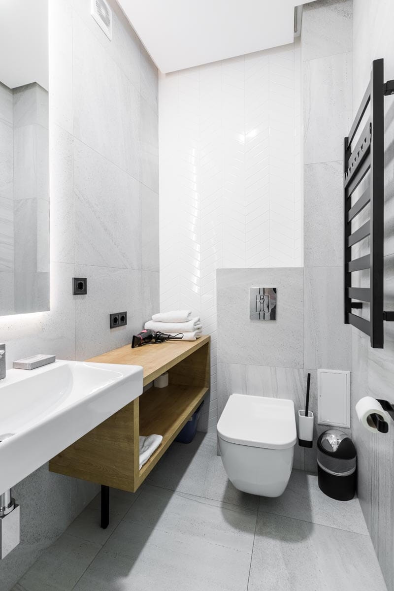 Kleines, modernes Gäste-WC in Grau-Weiß-Optik und Holz-Highlights mit Waschbecken und großem Spiegel links und Heizgitter für Handtücher rechts an der Wand.