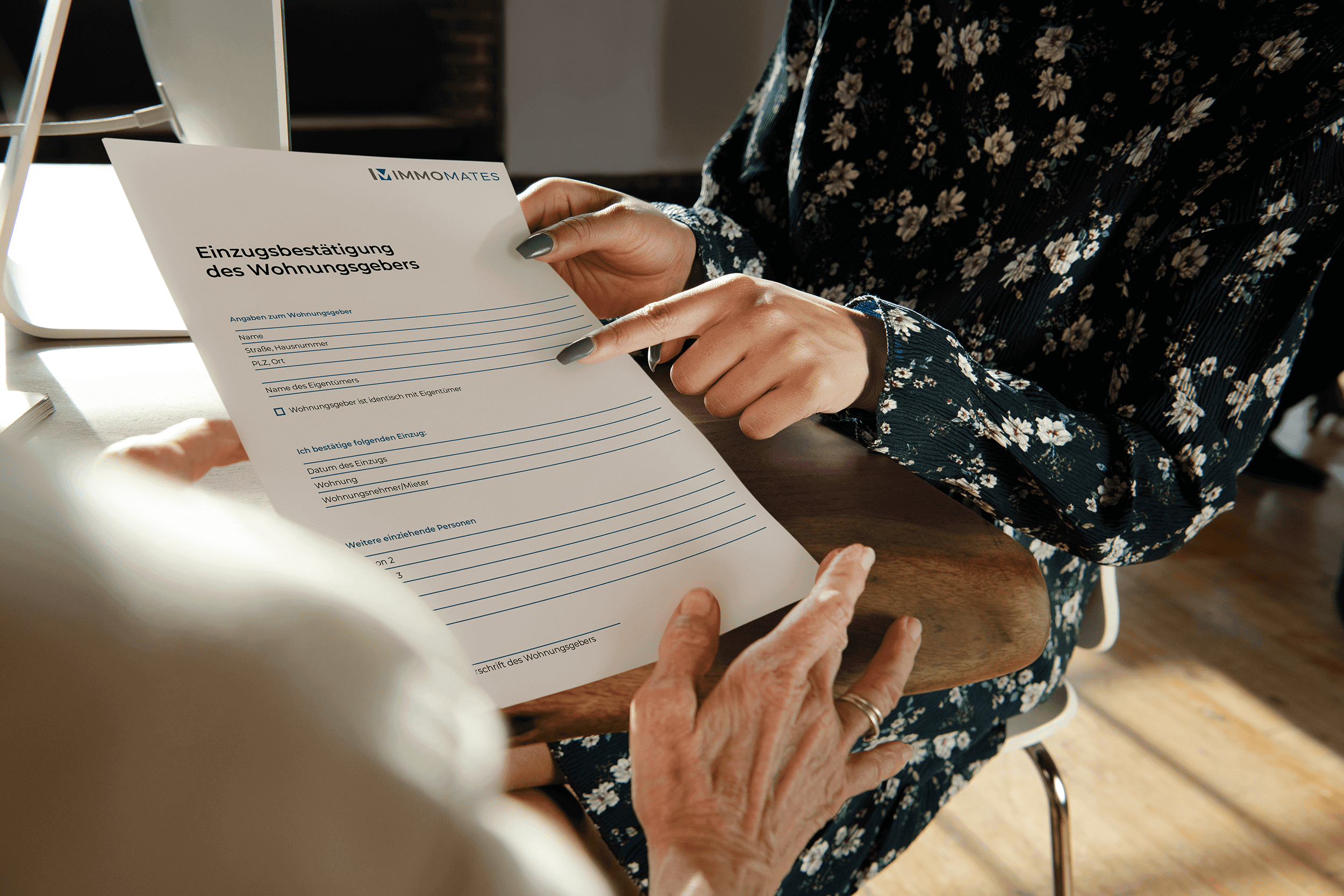 Eine Maklerin im geblümten Kleid zeigt einem Mandanten das Formular zur Einzugsbestätigung des Wohnungsgebers und zeigt mit dem Zeigefinger auf den Text.