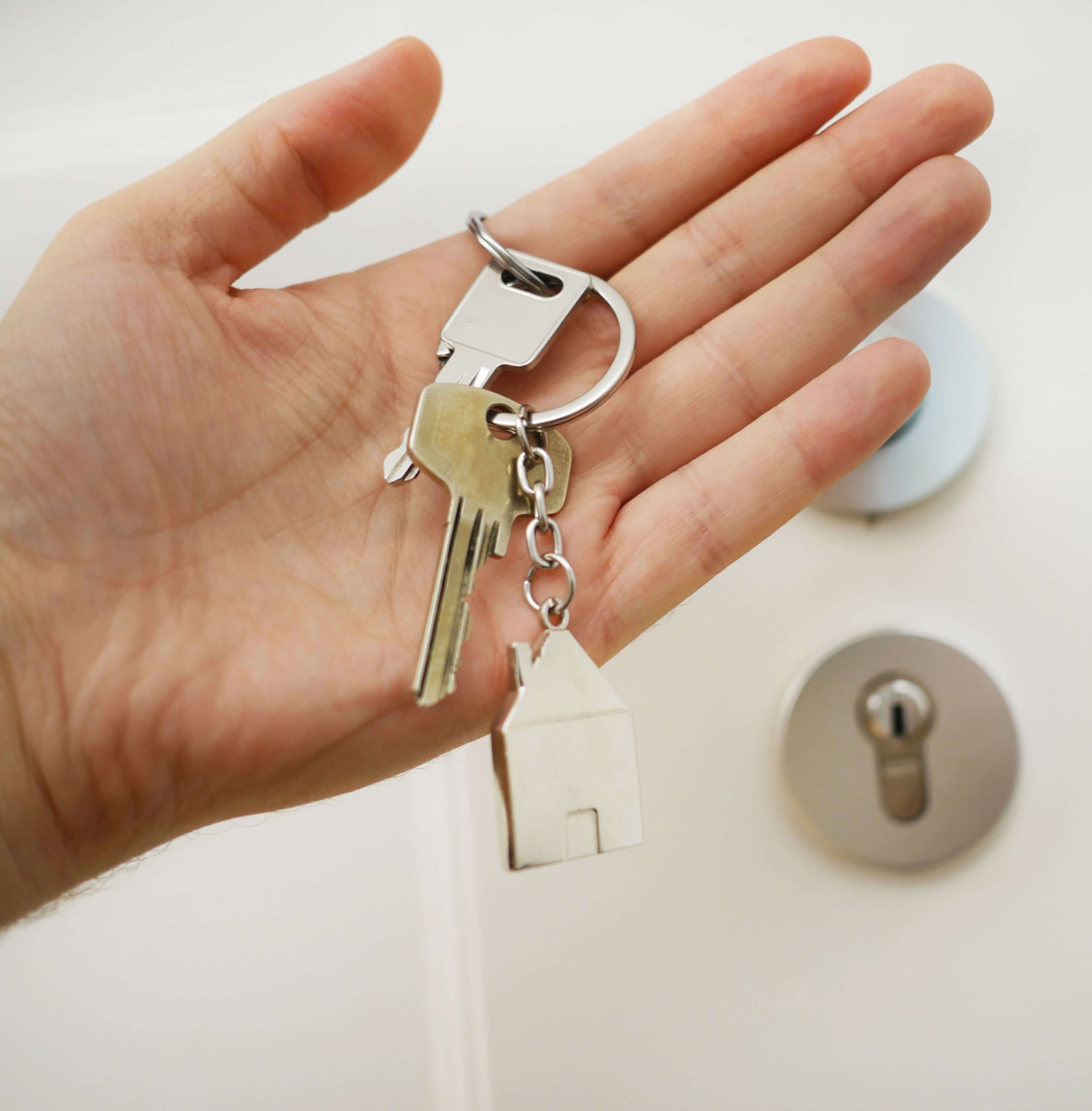Nahaufnahme einer Hand, in deren Innenfläche ein Wohnungsschlüssel an einem Schlüsselring mit einem Schlüsselanhänger in Form eines Häuschens liegt.