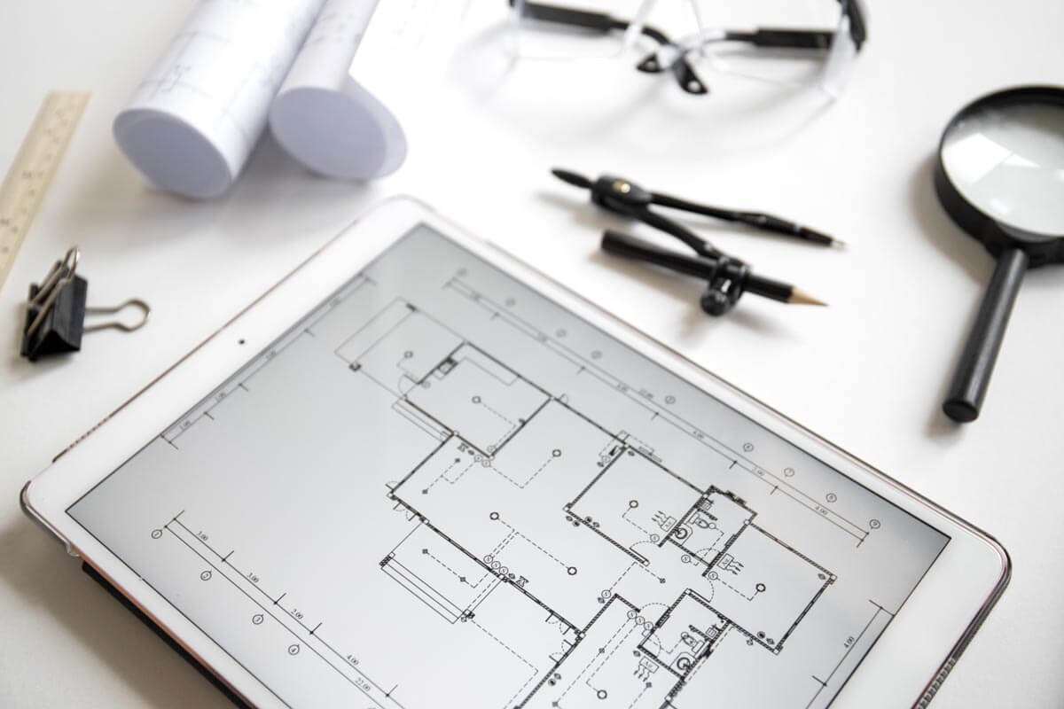 Tablet mit Bauplan auf dem Display und drumherum mehreren Utensilien zum Zeichnen eines Grundrisses von Hand.