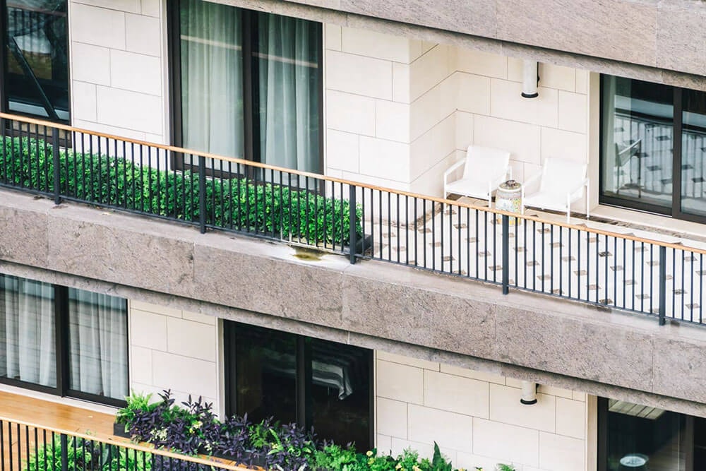 Detailansicht eines Balkons an einem Reihenhaus mit hellen Mauersteinen und leichter Begrünung und großen Fenstern