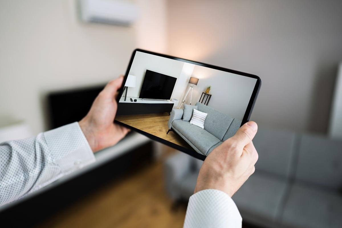 Eine Person nimmt mit einem mit beiden Händen erhobenen Tablet ein Foto des Wohnzimmers auf.