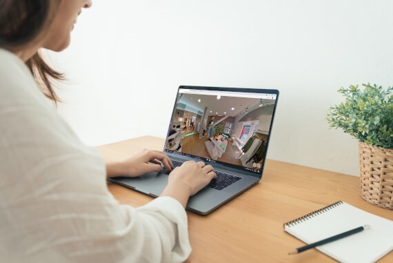 Blick über die Schulter einer Frau, die an einem Schreibtisch sitzt und im Tablet den 360 Grad Rundgang eines Bekledungsgeschäfts betrachtet.