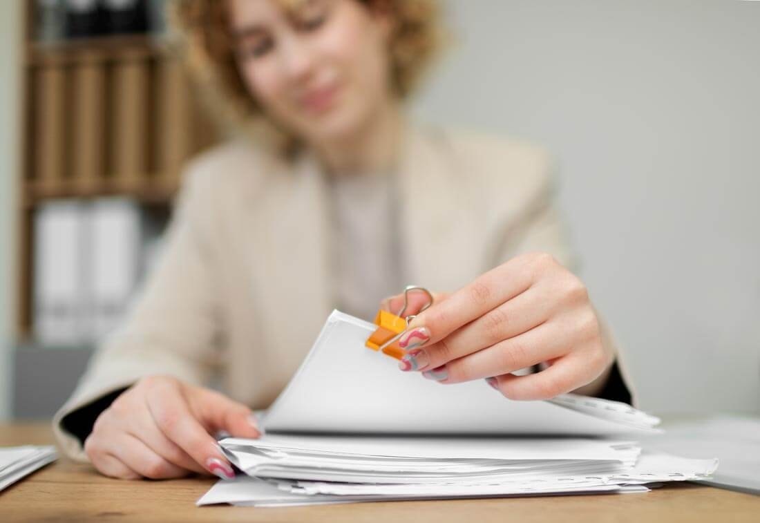 Nahaufnahme, wie eine Maklerin die zusammengehefteten Unterlagen vom oberen Ende eines Papierstapels nimmt.