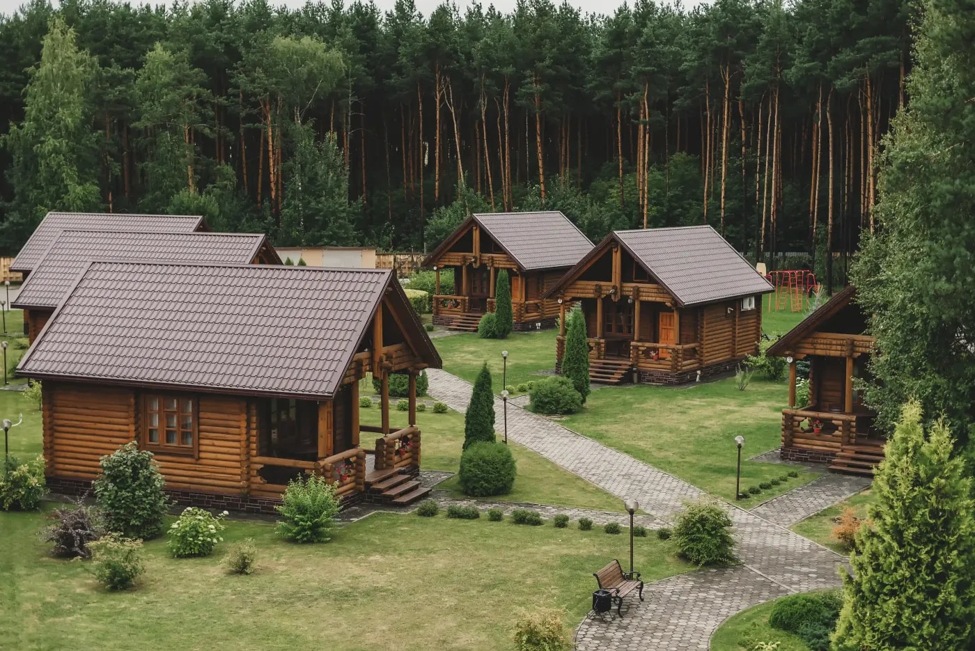 Gruppe baugleicher Holzbungalows mit Satteldach auf einer Lichtung in einem Kiefernwald.