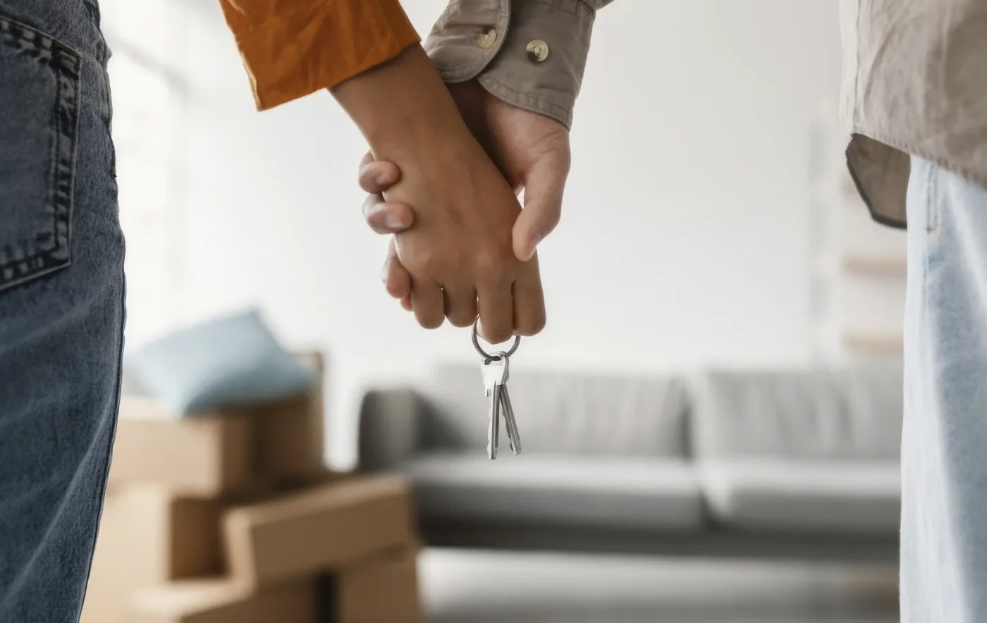 Nahaufnahme von den verschlungenen Händen eines Pärchens, die einen Wohnungsschlüssel halten.