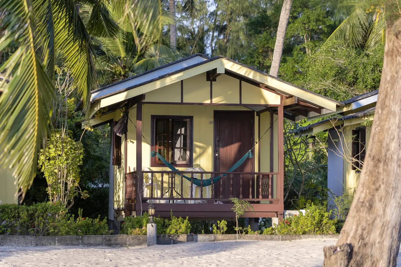 Frontansicht eines Tiki-Bungalows zwischen Palmen und Bambus am Strand.