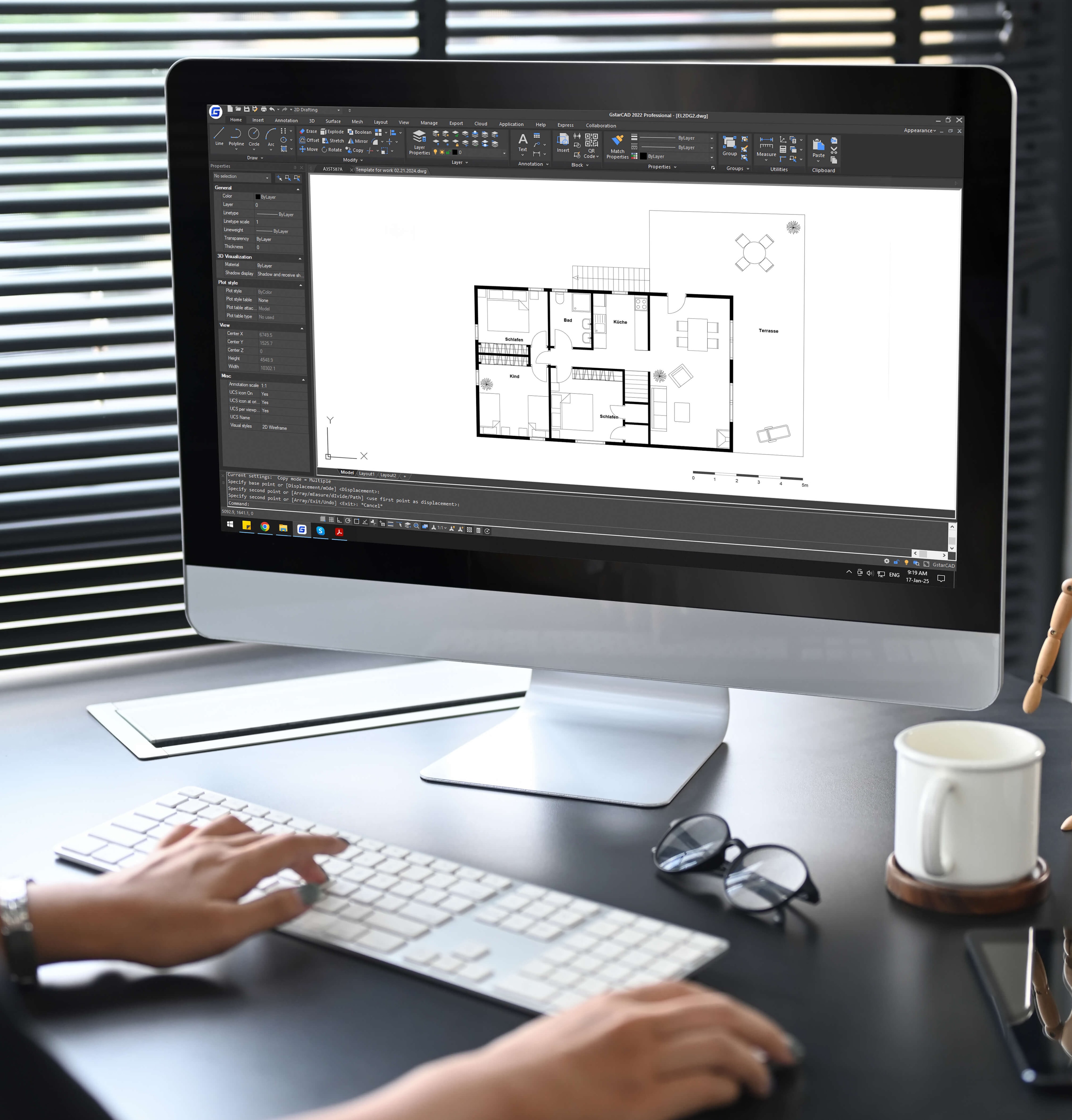 Eine Person arbeitet amit einer CAD-Software an einem detaillierten Grundriss mit beschrifteten Räumen, daneben Tastatur, Brille und Kaffeebecher auf dem Schreibtisch