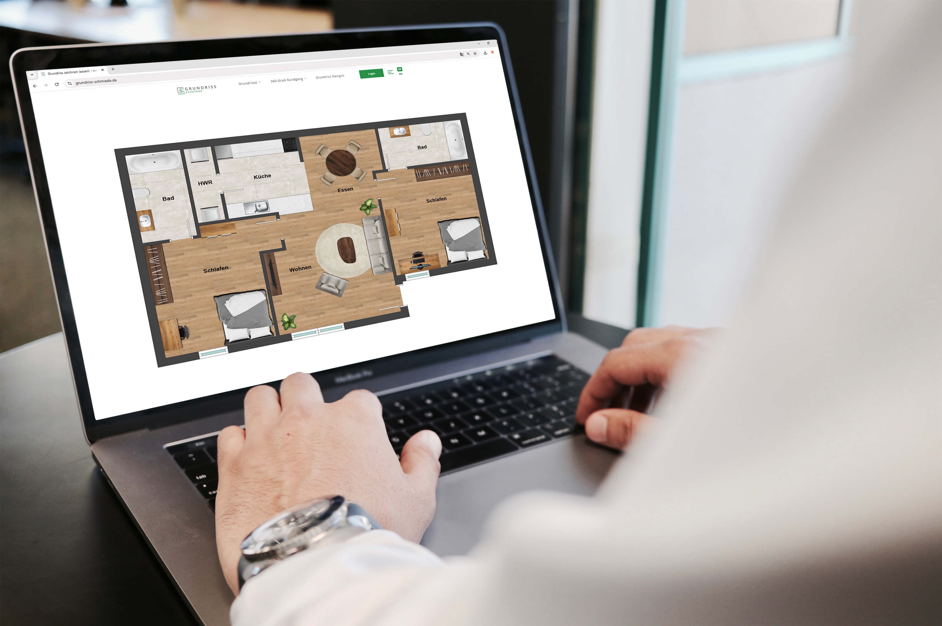 Blick am Arm eines Mannes vorbei auf den Bildschirm eines Laptops, auf dem der moderne Grundriss einer 2,5-Zimmer Wohnung zu sehen ist, mit offenem Wohn- und Essbereich, offener Küche und einem Hauswirtschaftsbereich.