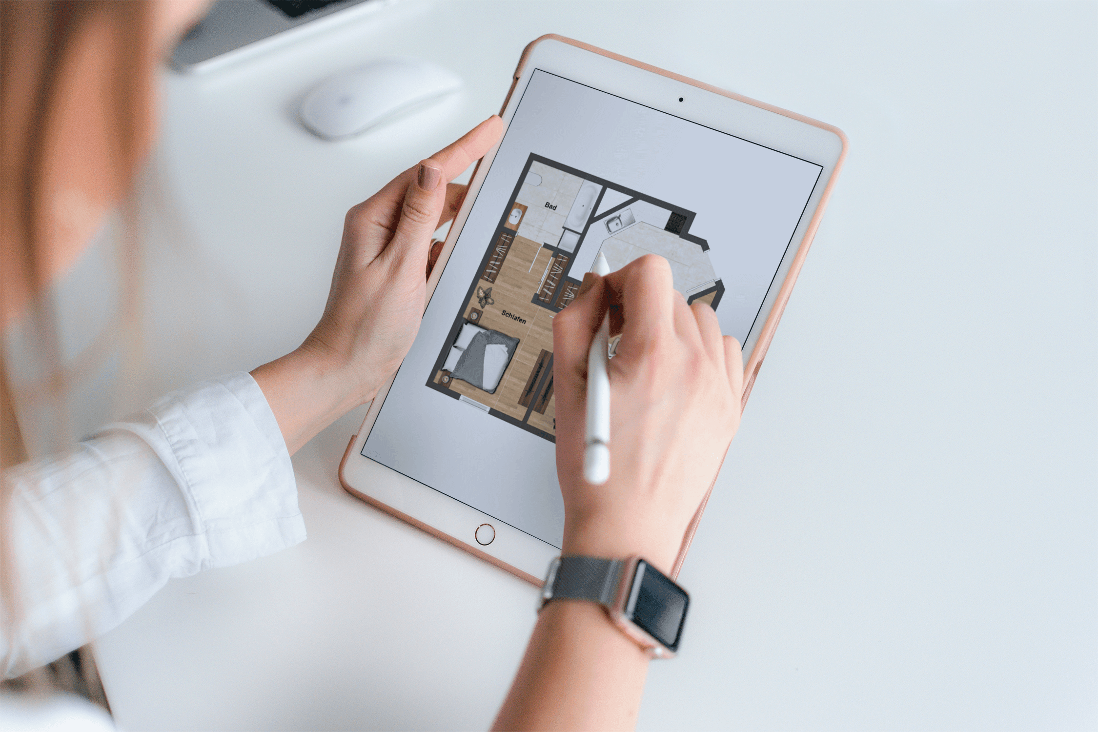 Blick über die Schulter einer Grafikerin, die mit einem Tabletstift den Grundriss einer 2-Zimmer Wohnung mit offener Küche im Tablet bearbeitet.
