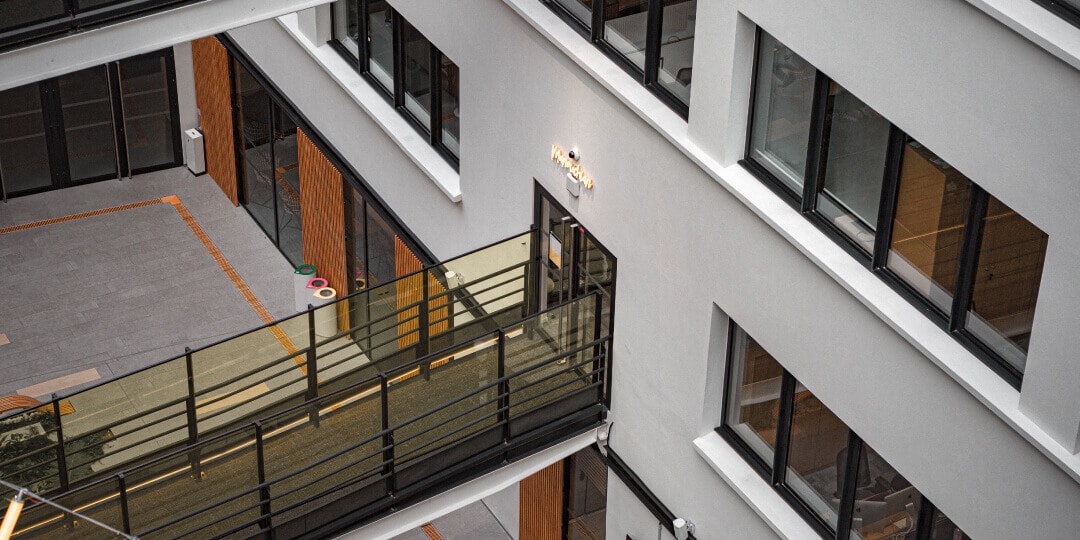 Vogelperspektive auf den Innenhof eines modernen Bürogebäudes mit verglastem Laufsteg und Holzpanelen.