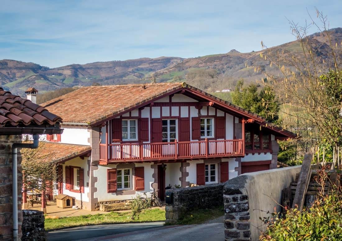 Typische Bergunterkunftshütte im Fachwerkstil mit flachem Satteldach, Balkon und Holzfensterläden vor spätsommerlicher Berglandschaft.