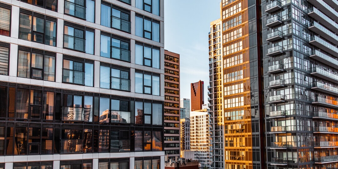 Blick zwischen modernen Hochhäusern mit Glas- und Balkonfassaden in einer Großstadt, seitlich von der Abendsonne beleuchtet.