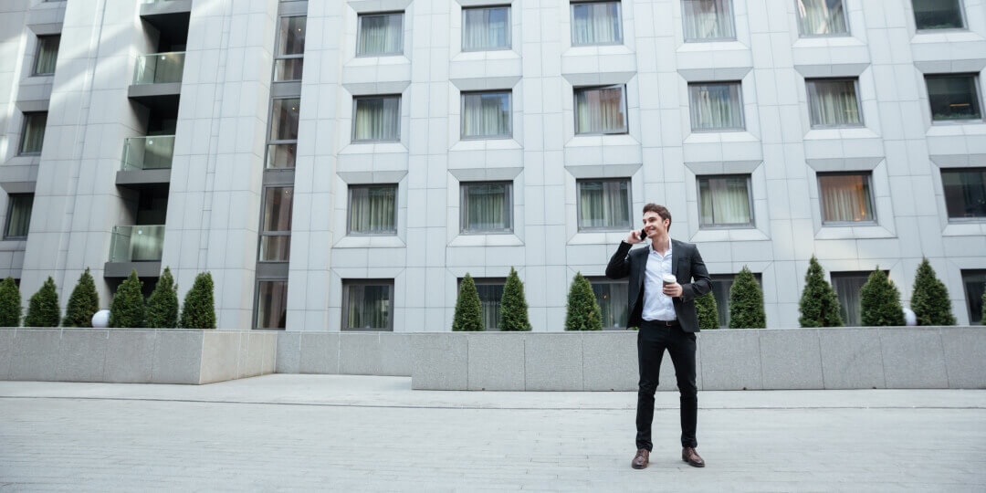 Mann im Anzug telefoniert vor einem modernen Gebäude mit markanter geometrischer Fensterfassade.