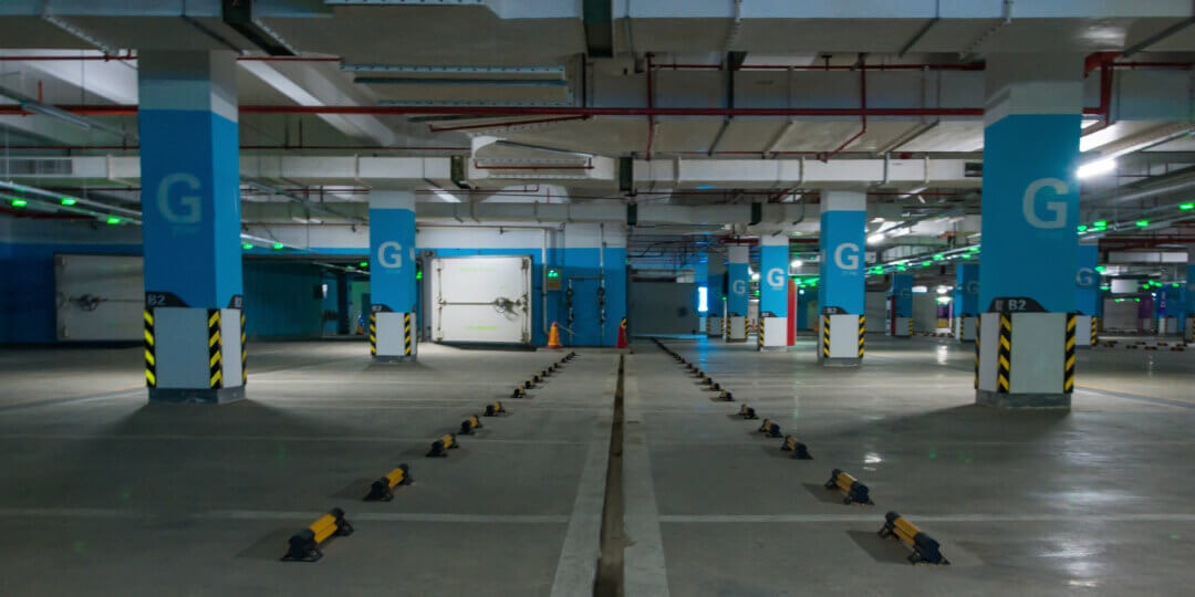 Leere Tiefgarage mit blauen Betonstützen, Stellplatzmarkierungen und gesicherten Parkbügeln auf dem Boden.
